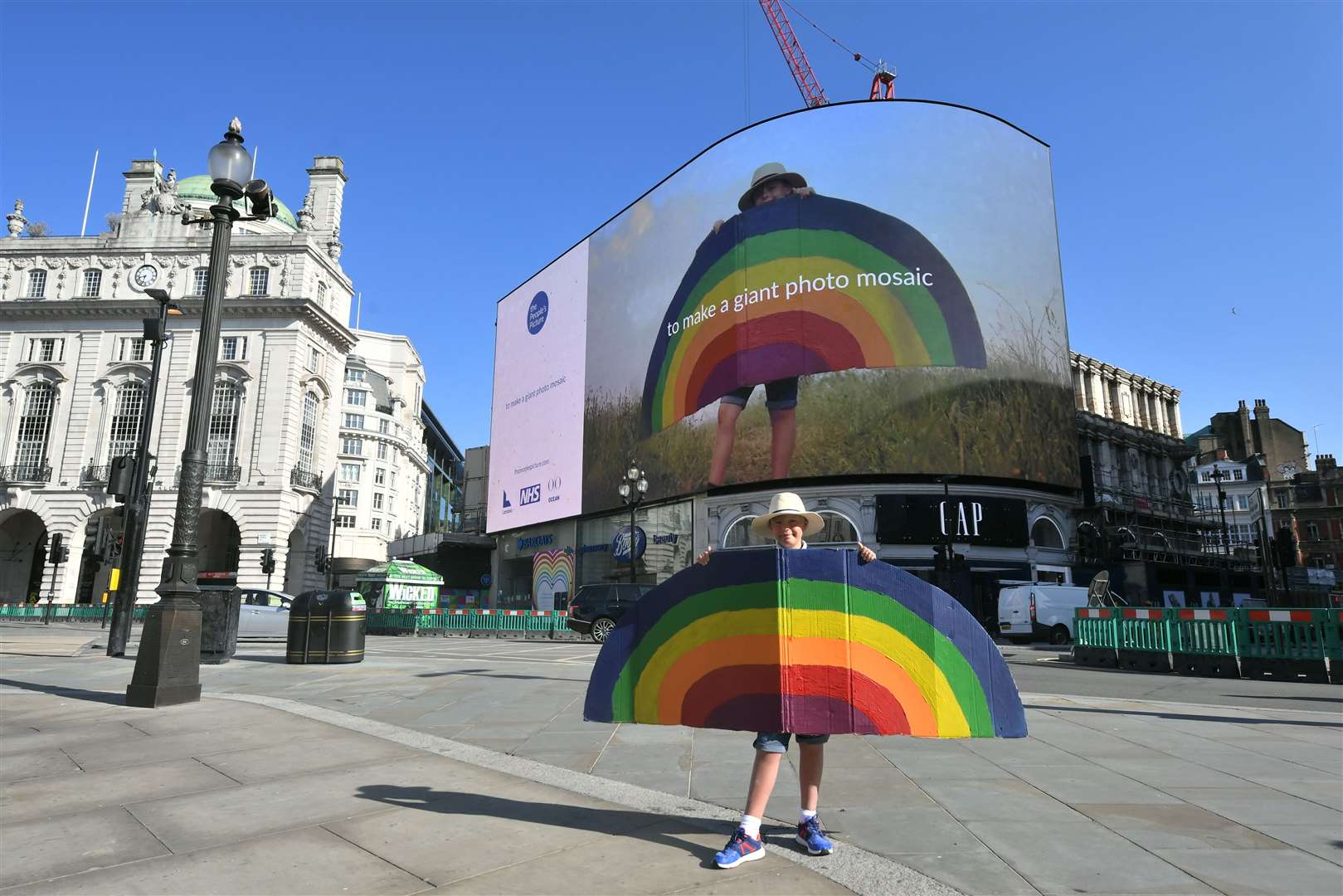 A participant holds a rainbow beneath the photo of himself on Piccadilly Lights (Dominic Lipinski/PA)