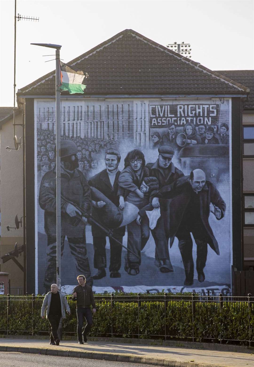 Two men walk past the Bloody Sunday mural that depicts the death of Jackie Duddy with Father Edward Daly, later Bishop Daly, waving a white handkerchief (Liam McBurney/PA)