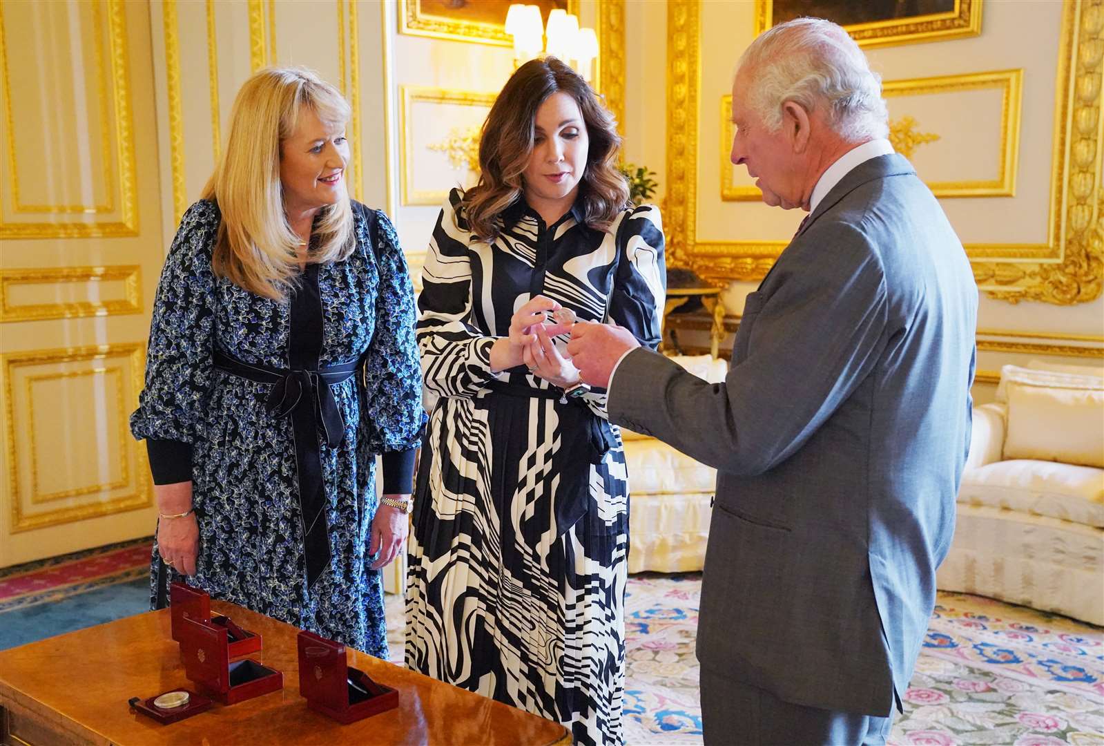 The King was presented with the first coronation coin struck by the Royal Mint by chief executive Anne Jessopp (left) and director Rebecca Morgan (centre) at Windsor Castle (Jonathan Brady/PA)