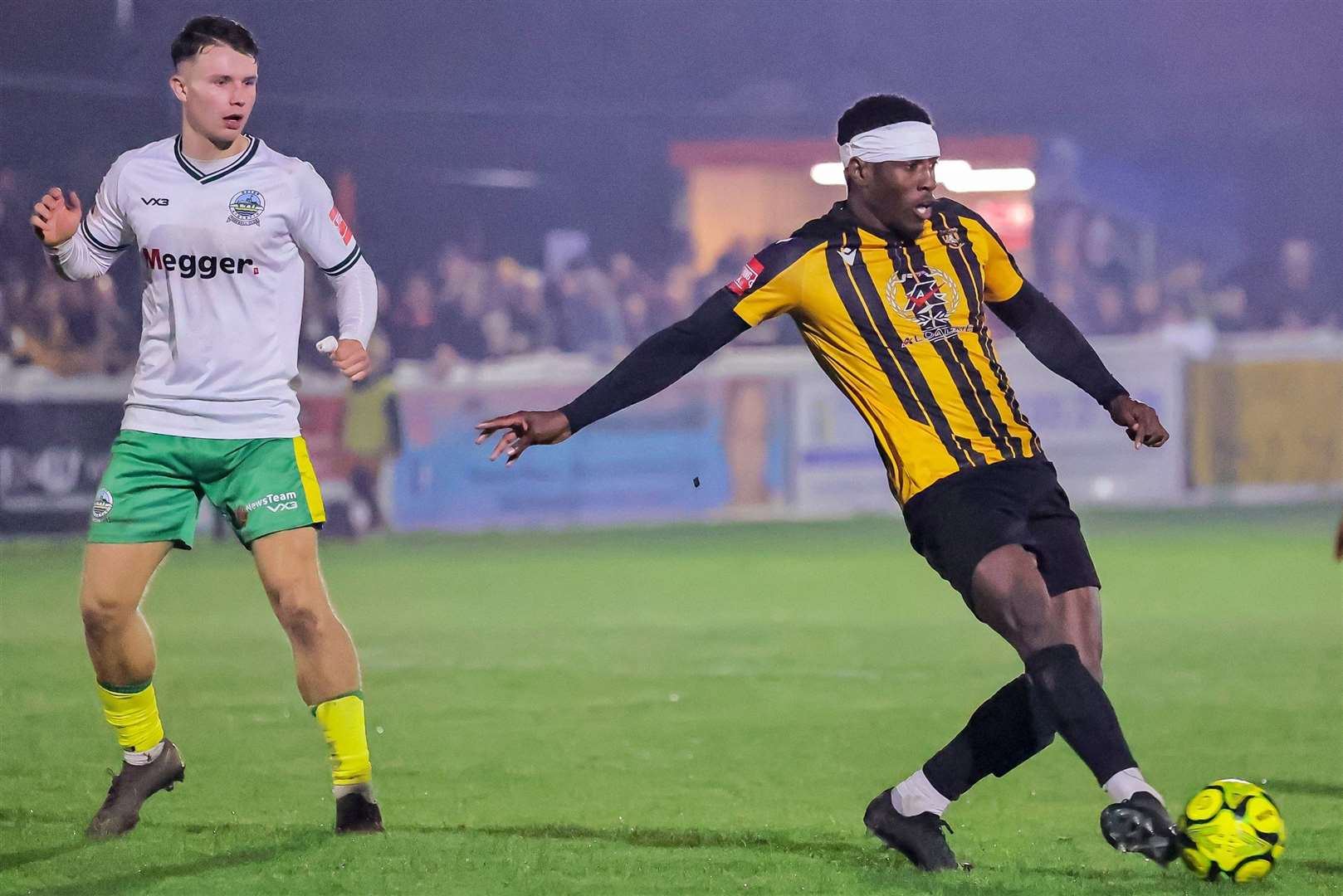 Folkestone defender Marvel Ekpiteta - bandaged up in Terry Butcher style - gets away from Dover's Harrison Pont. Picture: Helen Cooper