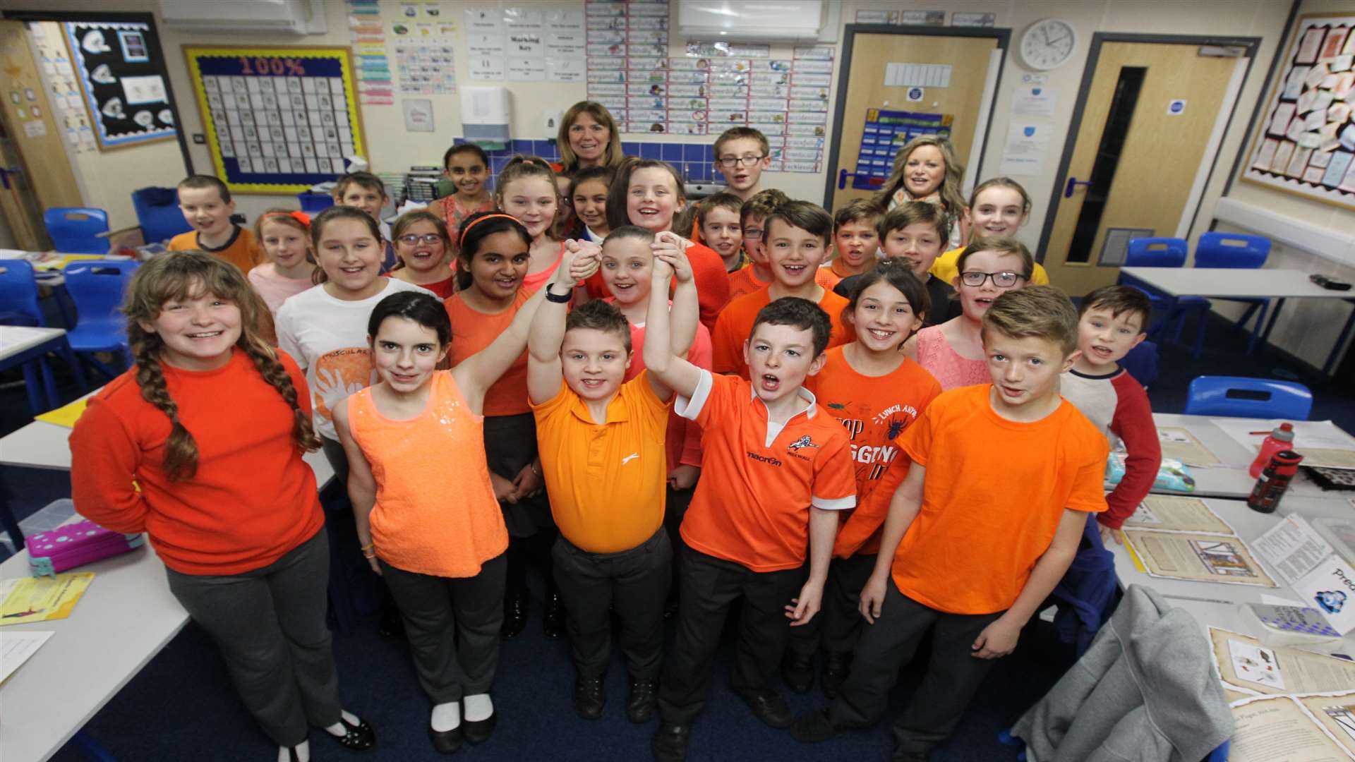 Classmates, wearing orange, hold up the arms of Adam,10 who has Duchenne Muscular Dystrophy.