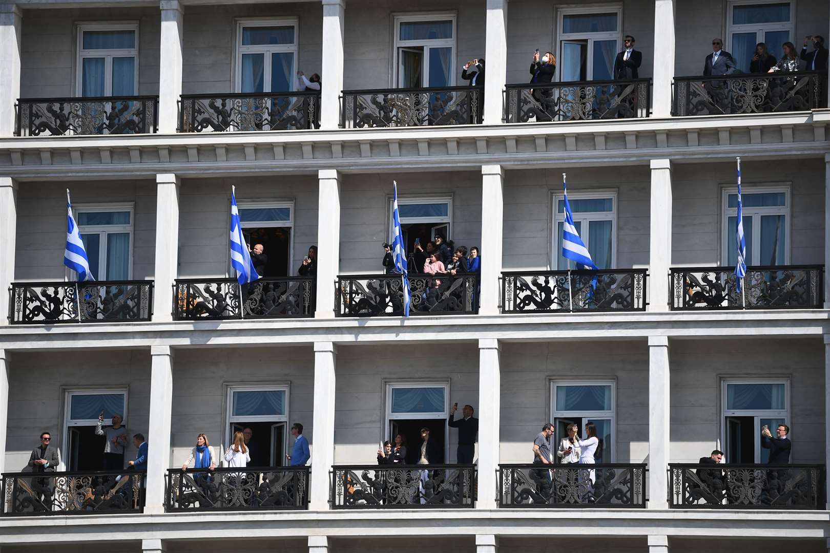 People watch from balconies of a building overlooking the Independence Day Military Parade in Syntagma Square (Victoria Jones/PA)