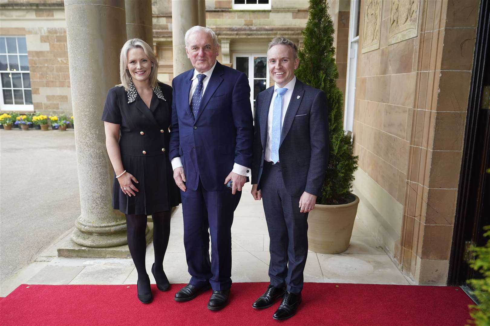 Former taoiseach Bertie Ahern is welcomed by Laura McCorry of Hillsborough Castle and Ryan Feeney, right, of Queen’s University at a Gala dinner to recognise Mo Mowlam’s contribution to the peace process and mark the 25th anniversary of the Good Friday Agreement (Niall Carson/PA)