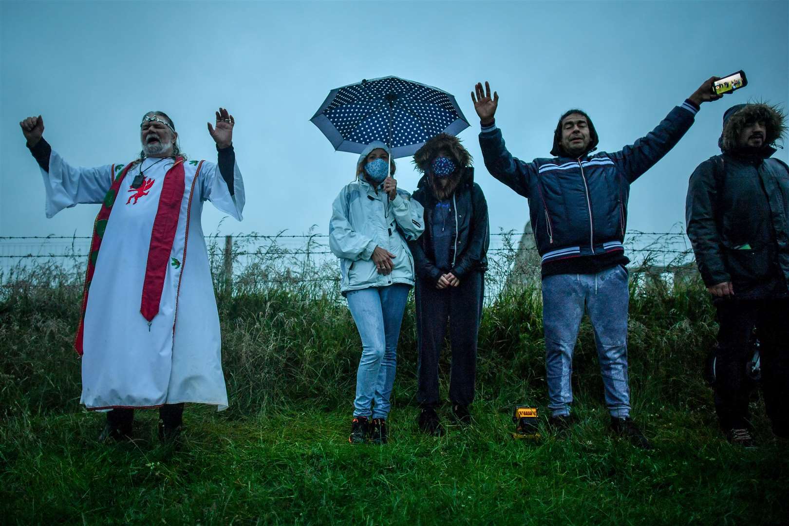 Arthur Uther Pendragon, left, and visitors turn to face the direction of the rising sun next to a closed Stonehenge on Sunday morning (Ben Birchall/PA)