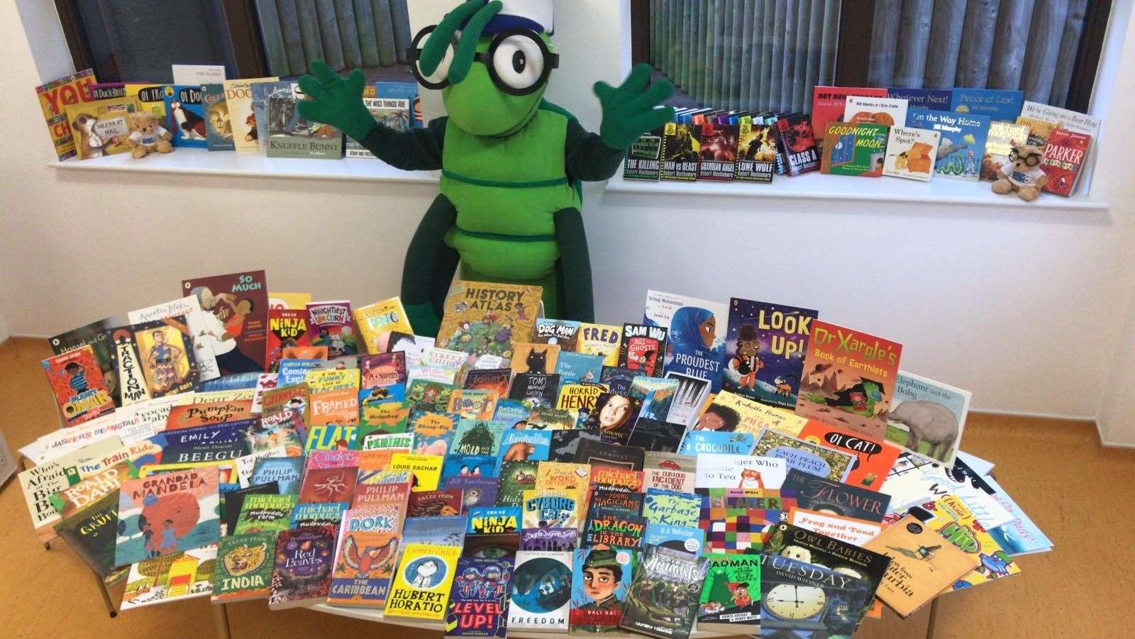 KM Charity Team mascot Buster Bug with the books donated by Scholastic Ltd.