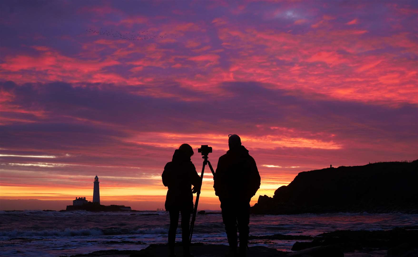 People takes photos of the colourful sky before sunrise at St Mary’s Lighthouse in Whitley Bay (Owen Humphreys/PA)