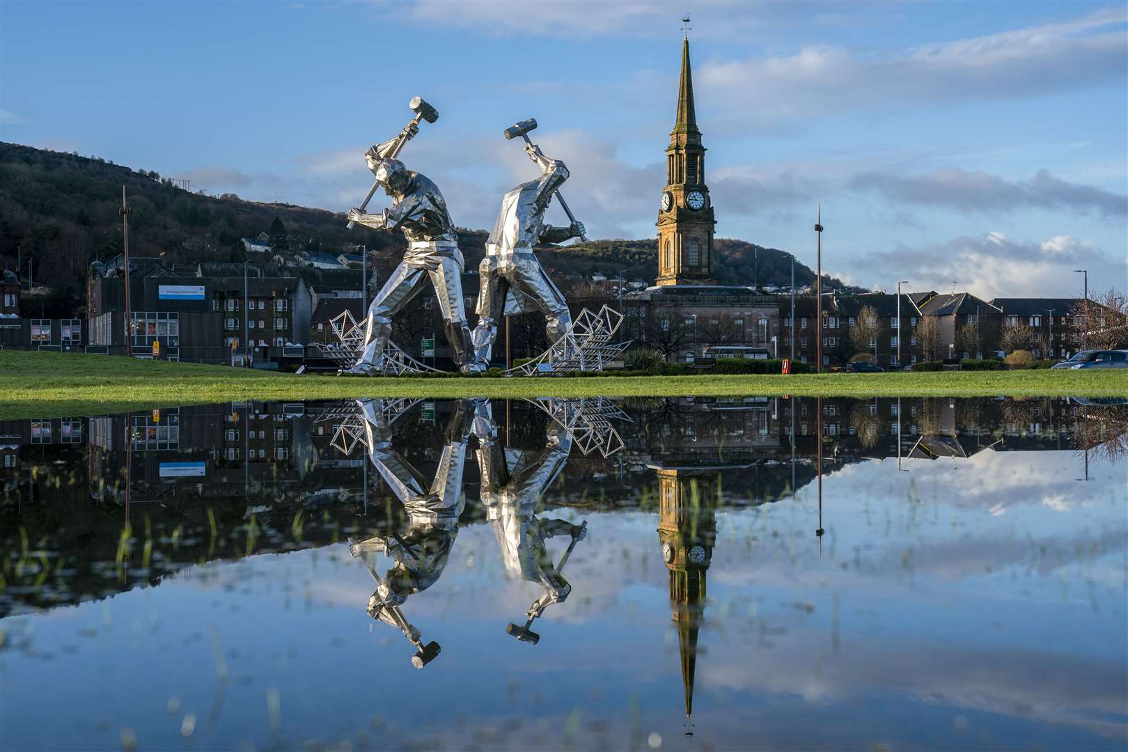 The Shipbuilders of Port Glasgow sculpture in Coronation Park, Inverclyde, is reflected in large puddles after heavy downpours (Jane Barlow/PA)