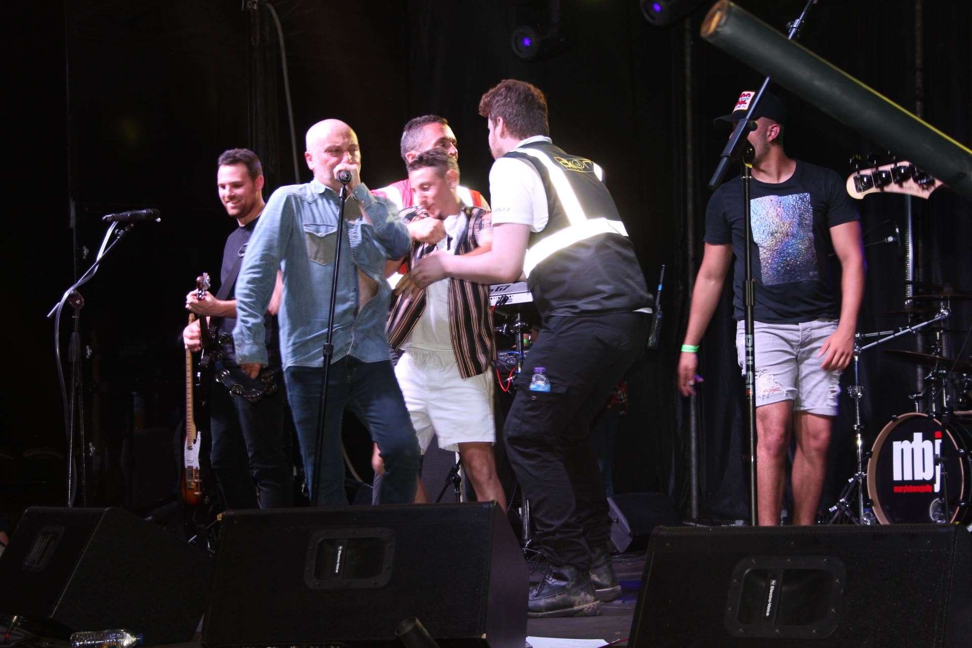 The stage invader is dragged away after grabbing Ed Austin of Marylebone Jelly at Sittingbourne's Party in the Park on Saturday. Picture: John Nurden (13188246)