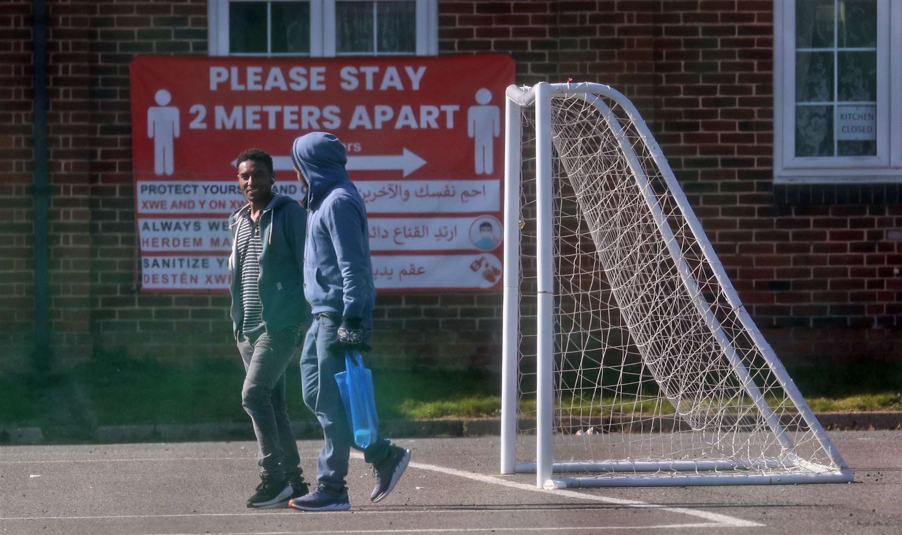 Two men walk past signs erected at the barracks as people return to the site following an outbreak of Covid-19 (PA)