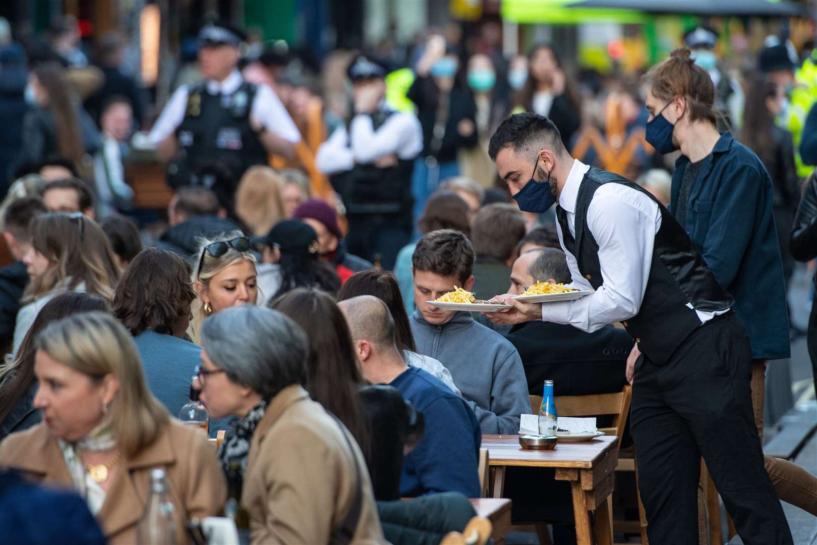 Waiters serve people eating and drinking at outside tables in Soho (PA)