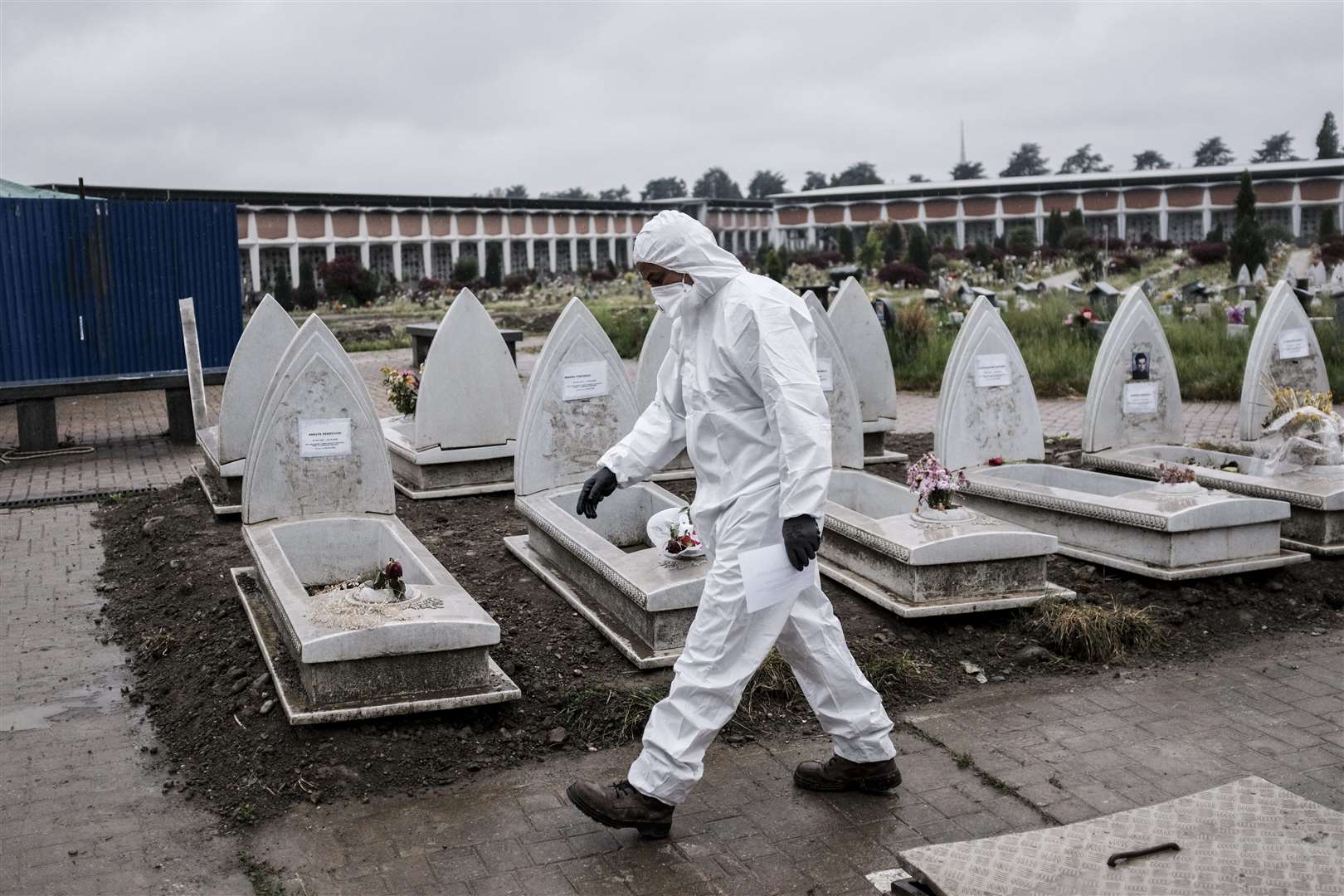 A man wearing a protective outfit walks past headstones at the Monumental cemetery in Turin, Northern Italy (Marco Alpozzi/AP)