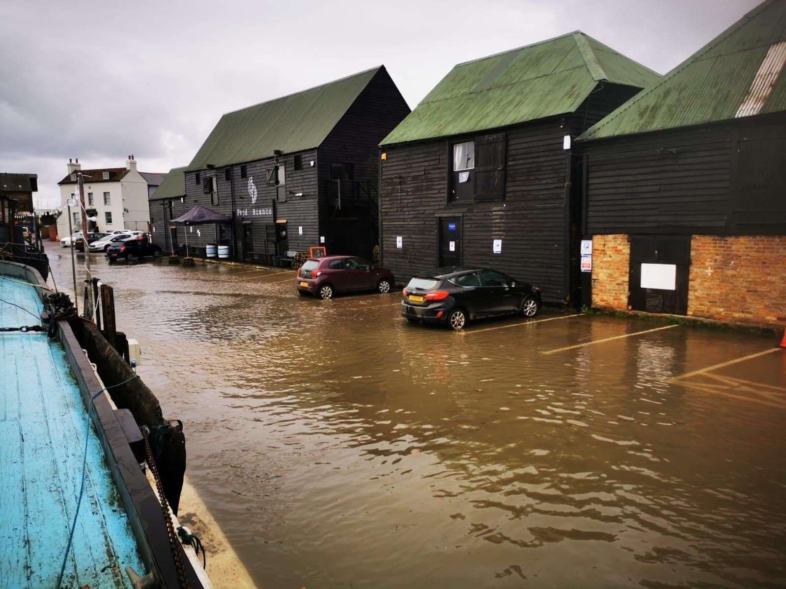 A photo taken earlier this afternoon shows water creeping up to cars and buildings by Faversham Creek. Picture: @GretaBarge1892/Twitter