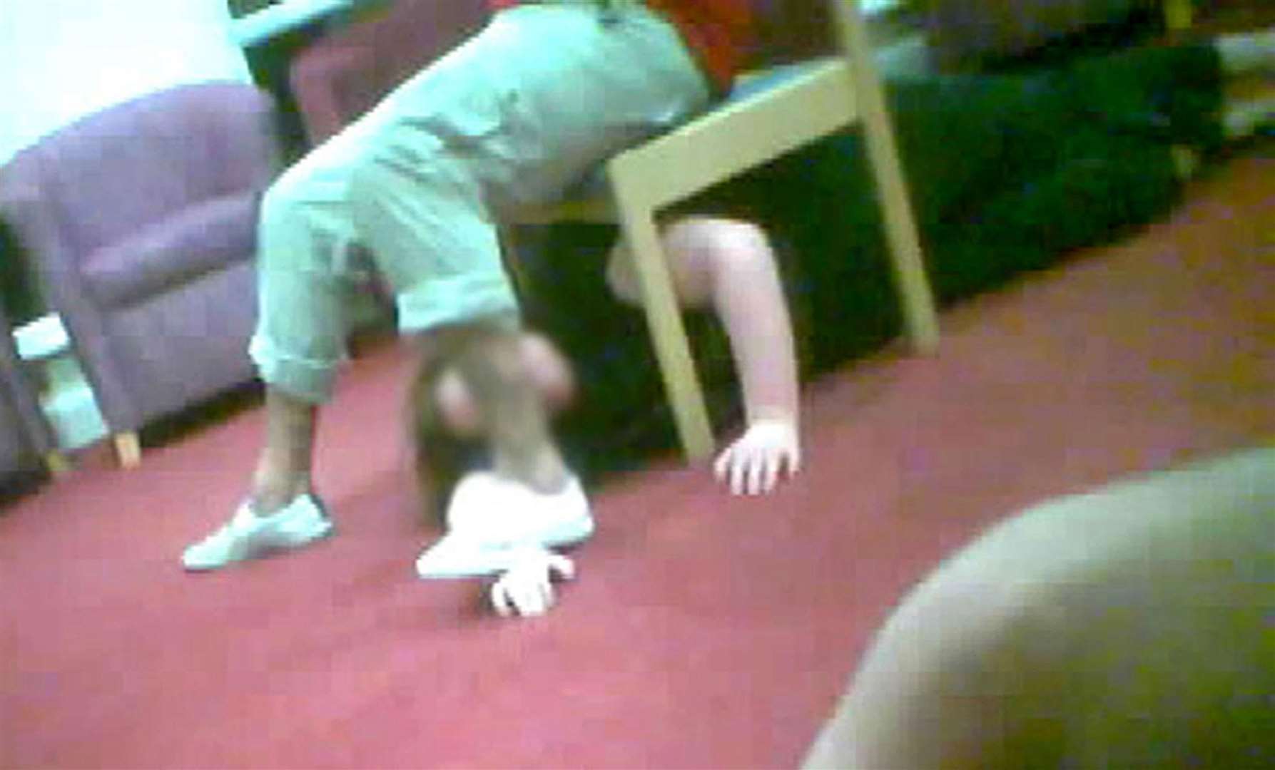 A care worker at Winterbourne View restraining a patient under a chair (BBC/PA)