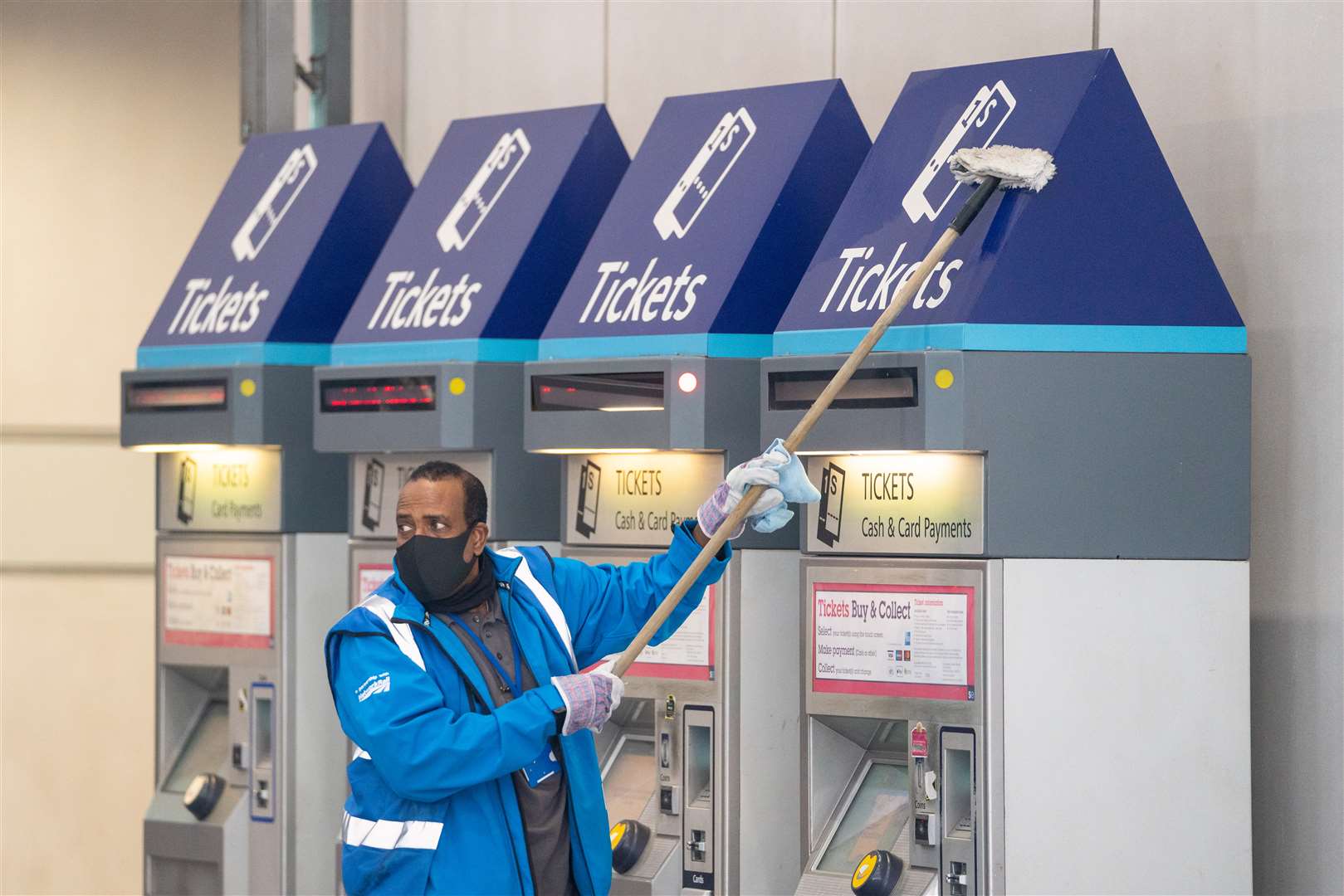 A member of staff wearing a protective face mask cleans ticket machines at London Bridge station (PA)