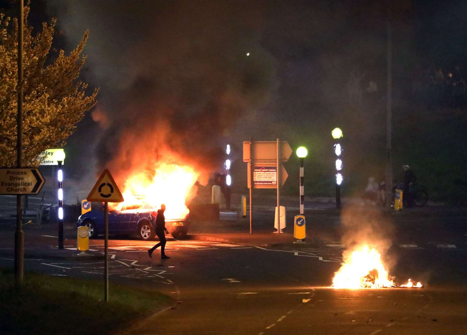 A man walks past a burning car that was hijacked by loyalists at the Cloughfern roundabout in Newtownabbey (Peter Morrison/PA)