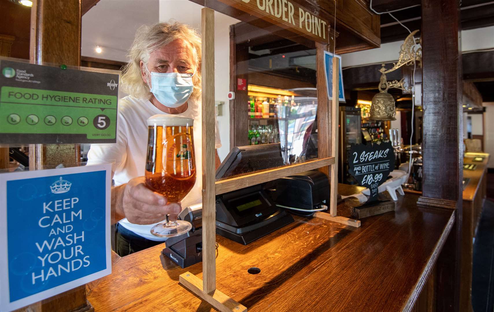 Phil Weaver, owner of The Old Smithy pub in Church Lawford, Warwickshire, serves a pint of beer from behind a protective screen (Joe Giddens/PA)