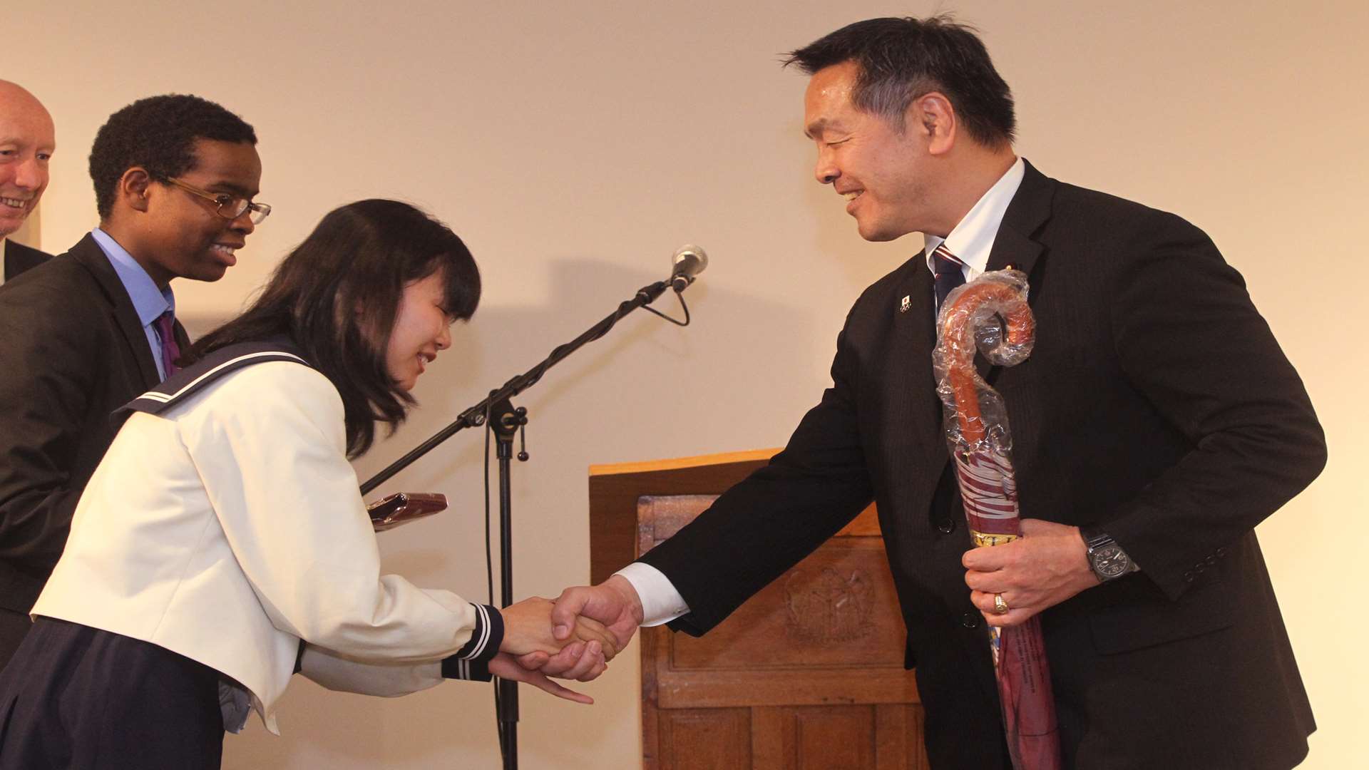 Mr Hase receives an umbrella and a school tie from Japanese exchange student Mika Maruyama, 17, and Japanese speaking Reme Iyore, 17, from Dartford Grammar.