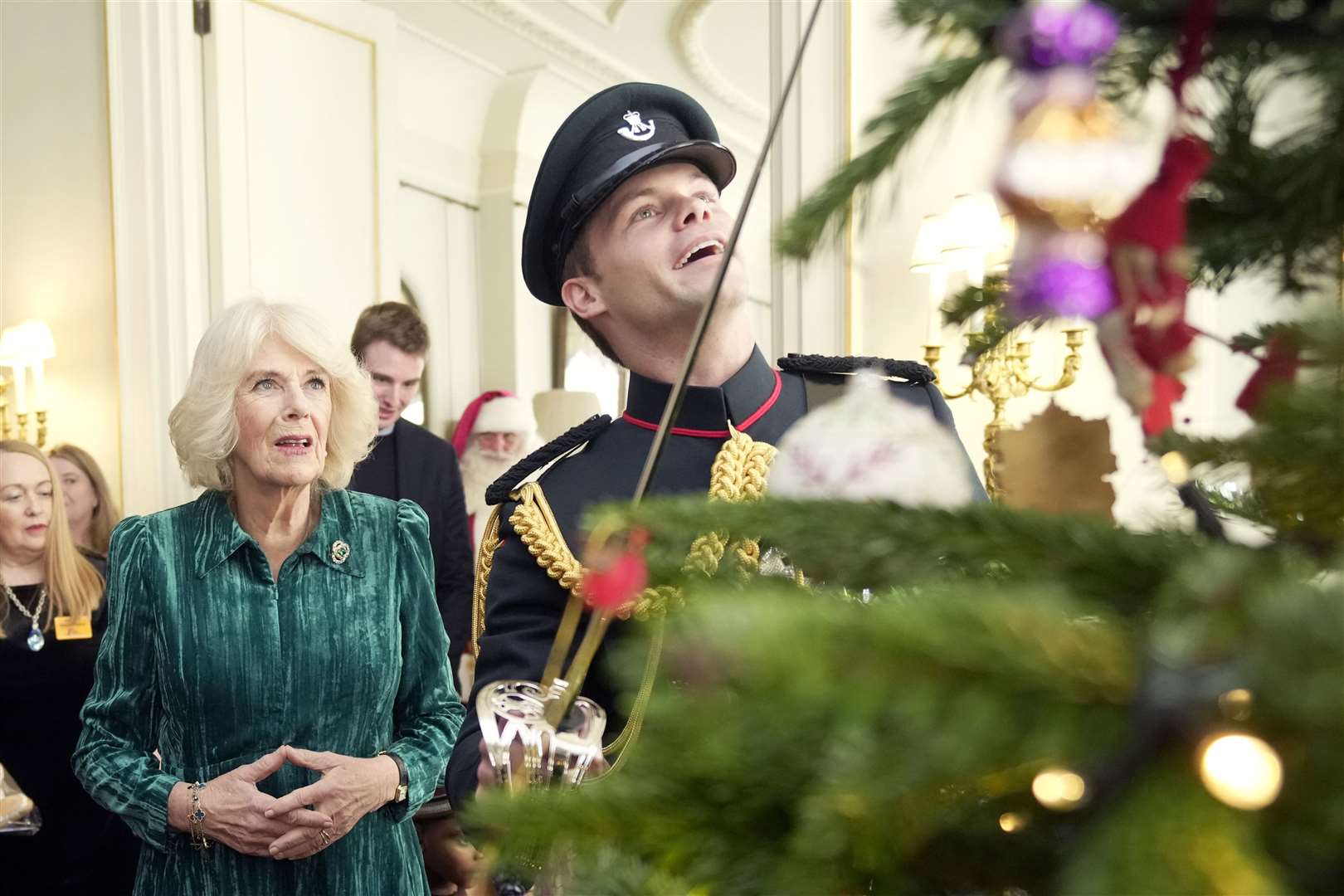 The Queen watches as her equerry places a decoration on the Christmas tree with his sabre (Kin Cheung/PA)