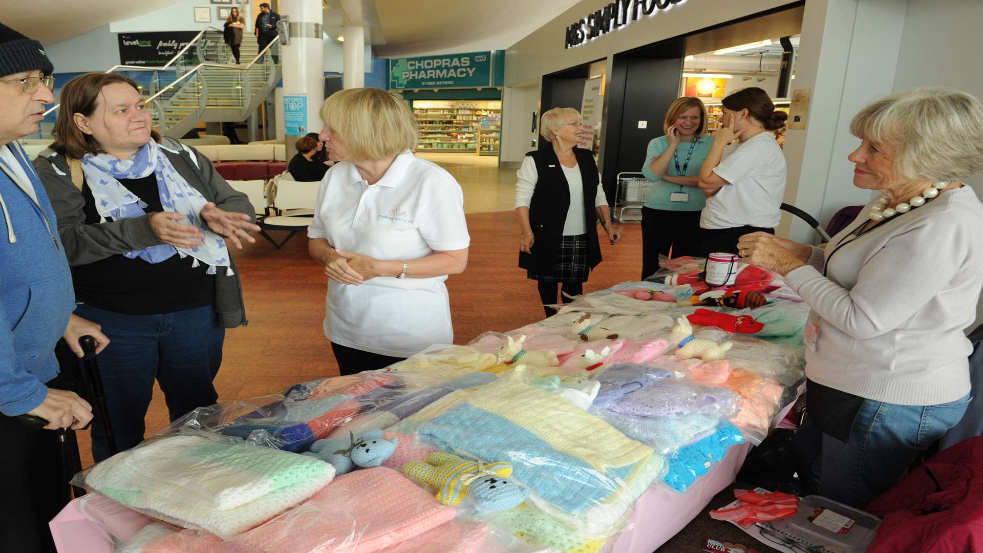 Darent Valley Hospital, Dartford. New Making Miracles charity stall in reception. Trish and Garry Chapman talk with Sally Howells (chairman) about knitting bedspreads for them.