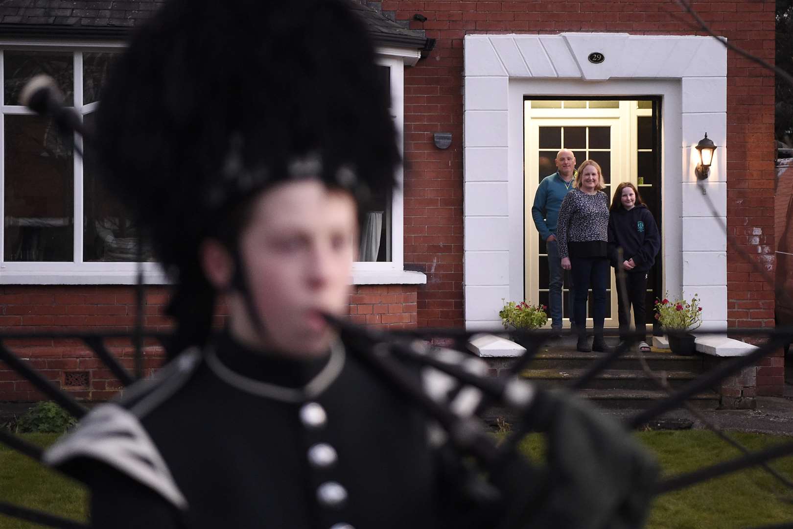 Healthcare worker Jill Scott, her husband Gordon and daughter Rececca listen as George Orchin plays Amazing Grace outside their front house in east Belfast (Michael Cooper/PA)