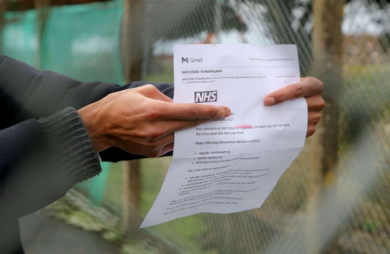 A man seeking asylum in the UK shows his negative NHS Covid-19 test result through the fence at Napier Barracks (Gareth Fuller/PA)