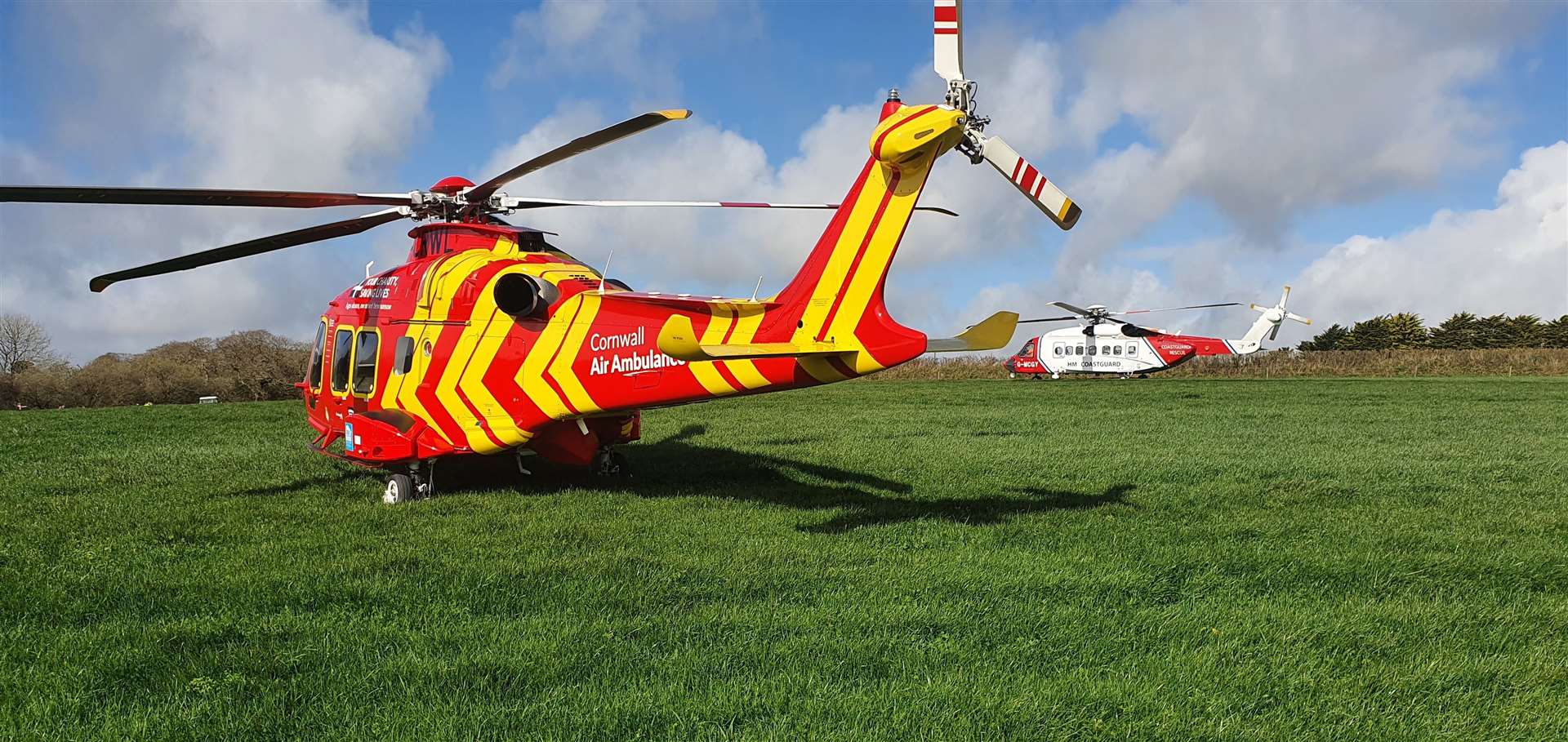 A Cornwall Air Ambulance helicopter alongside a Coastguard SAR helicopter in a field adjacent to where a Royal Navy Hawk jet crashed (Cornwall Air Ambulance/PA)