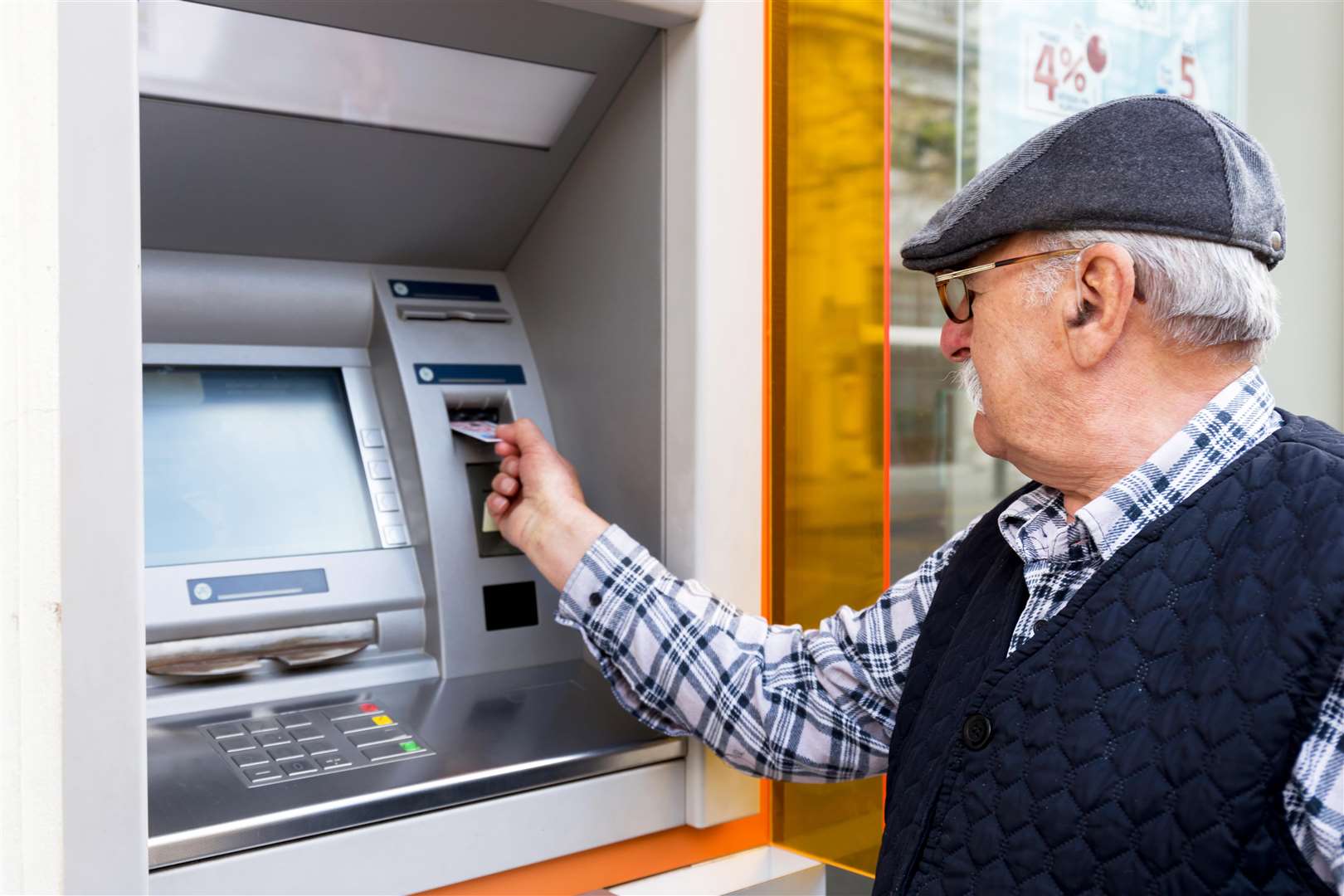 Elderly man inserting credit card to ATM outdoors. Stock image.