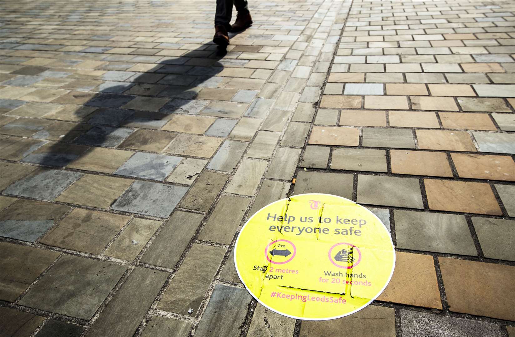 A person casts a shadow walking past a social distancing information sign painted on the pavement in Leeds city centre (Danny Lawson/PA)