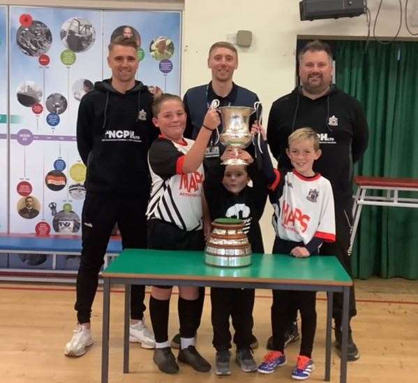 Sandown School pupils, pictured with Deal Town’s Tom and Ben Chapman, and manager Steve King, get their hands on the Southern Counties East League Premier Division trophy