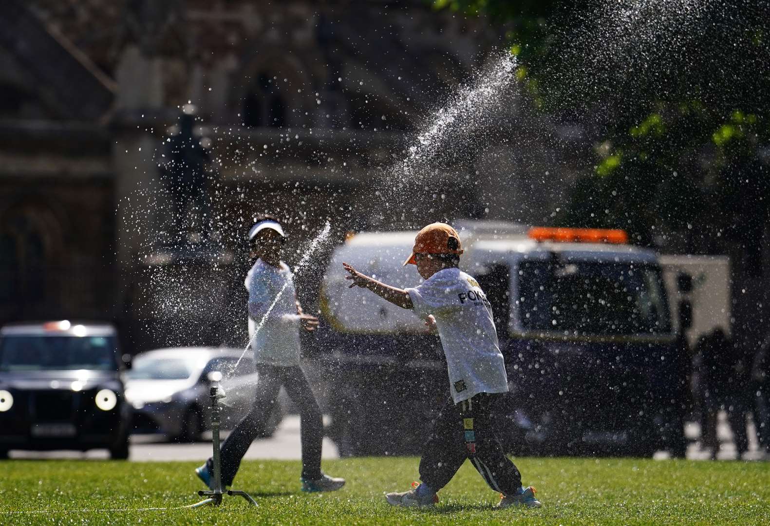 Children run through a sprinkler at Parliament Square in London (Jordan Pettitt/PA)