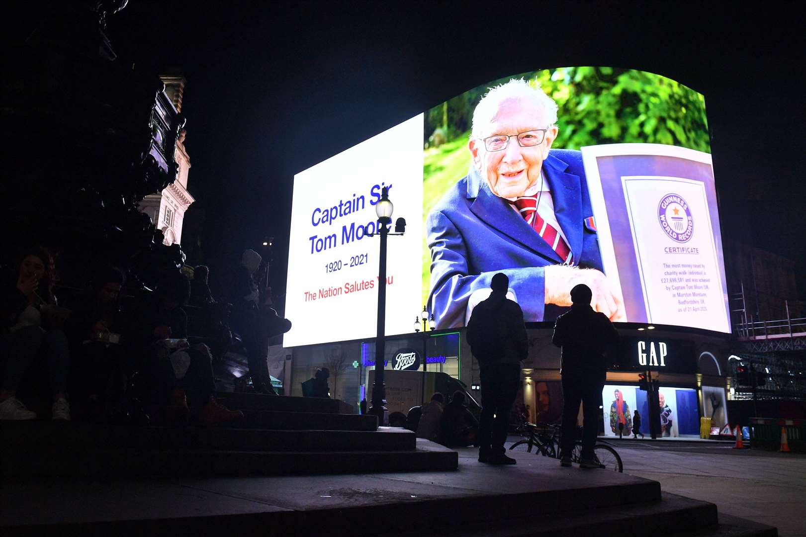 Members of the public stand in front of a tribute to Sir Tom at the Piccadilly Circus lights in central London as they joined in with the nationwide clap (Dominic Lipinski/PA)