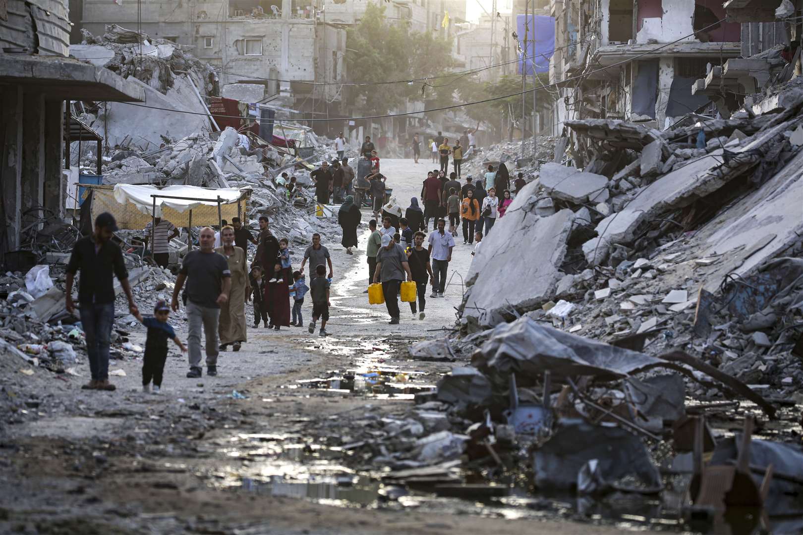 Palestinians displaced by the Israeli air and ground offensive on the Gaza Strip walk through sewage flowing into the streets of Khan Younis, Gaza (Jehad Alshrafi/AP)