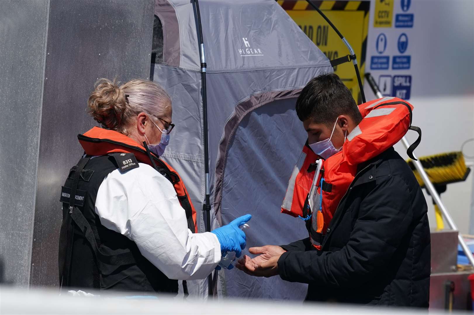 A man is given hand sanitiser by a Border Force officer as a group of people thought to be migrants are brought into Dover (Gareth Fuller/PA)