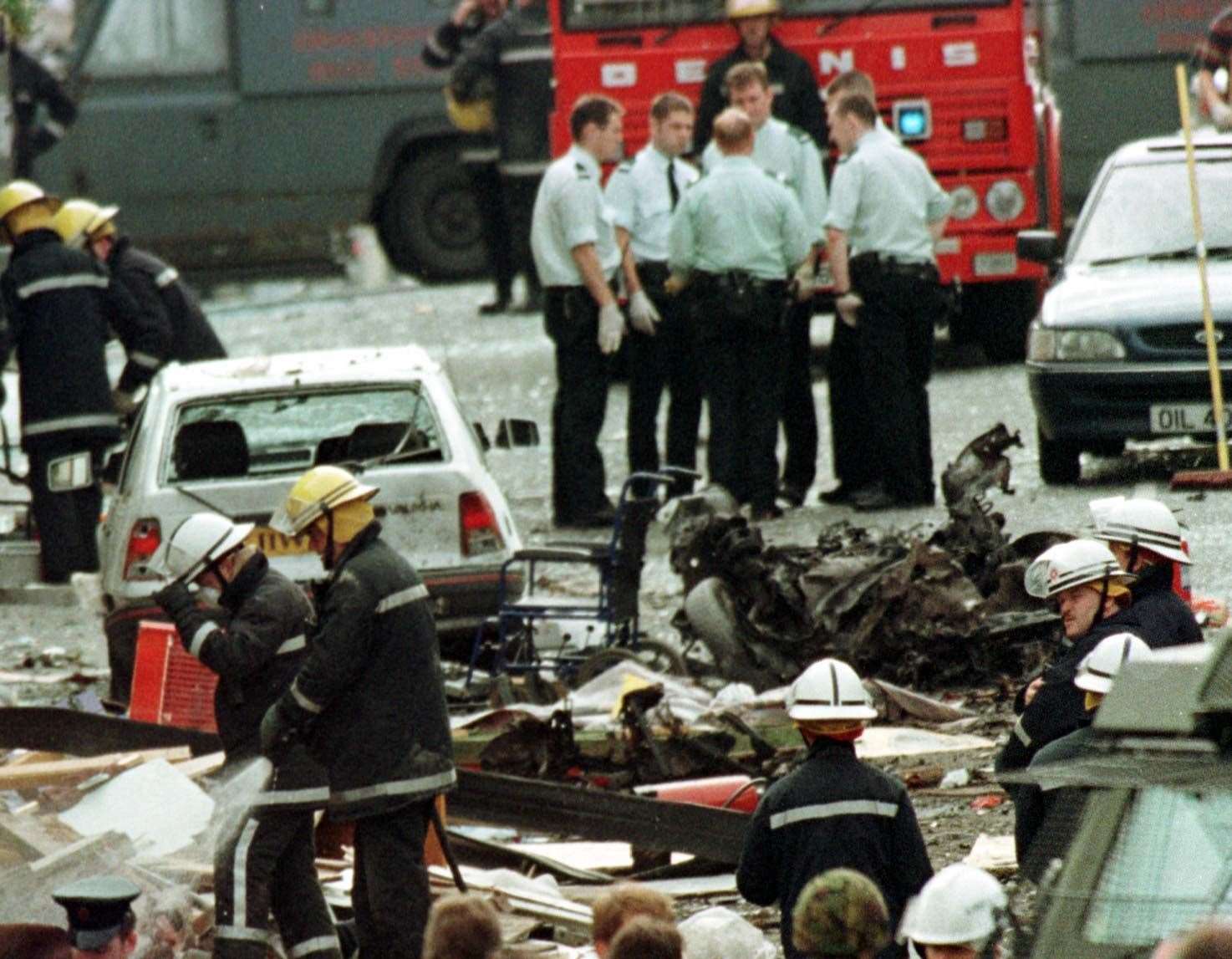 Royal Ulster Constabulary police officers and firefighters inspecting the damage caused by a bomb explosion in Market Street, Omagh, Co Tyrone (PA)