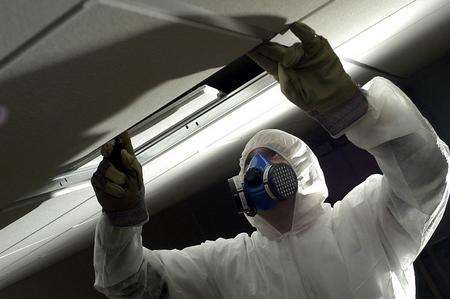 A health and safety inspector checks ceiling panels for asbestos.