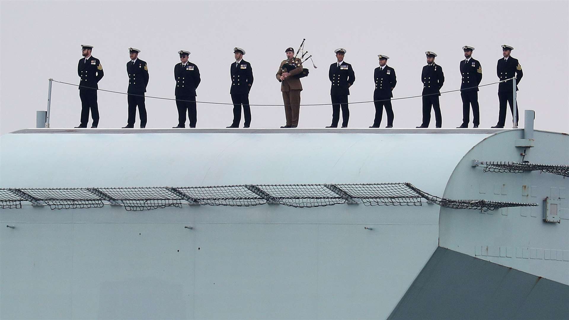 Ship’s company including a piper stand on the ski ramp of the Royal Navy aircraft carrier (Andrew Matthews/PA)