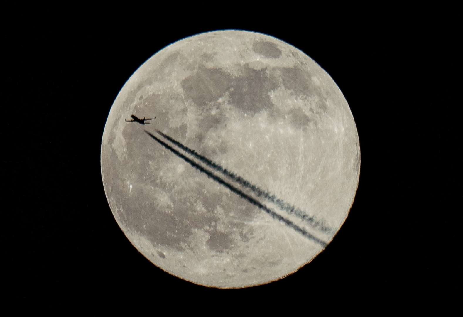 A plane flies past the moon over London (Aaron Chown/PA)