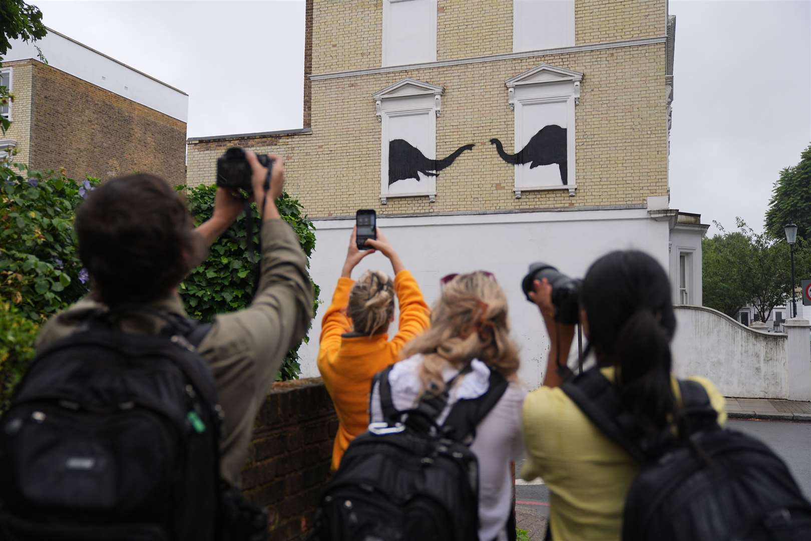 People photograph the Banksy depicting two elephants poking their heads out of blocked out windows (Yui Mok/PA)