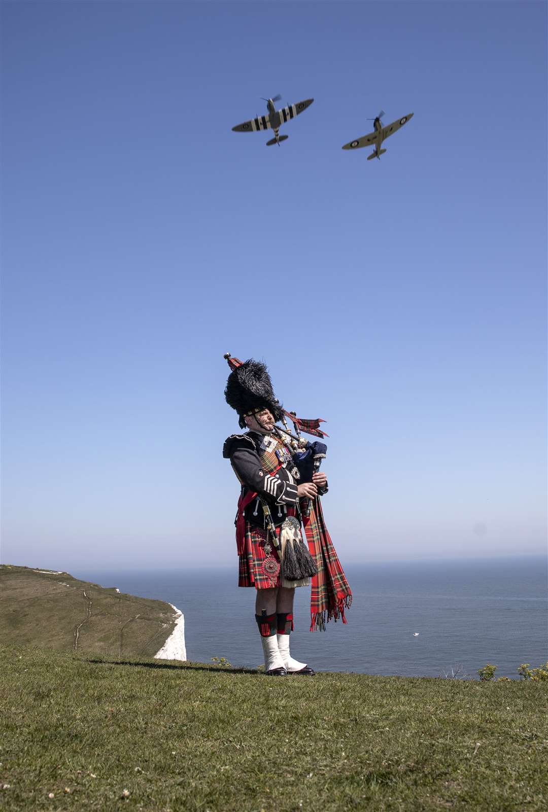 Pipe major Andy Reid of The Scots Guards plays his pipes on the cliffs of Dover as two Spitfires from the Battle of Britain memorial flight fly overhead on Thursday (Richard Pohle/The Times/PA)