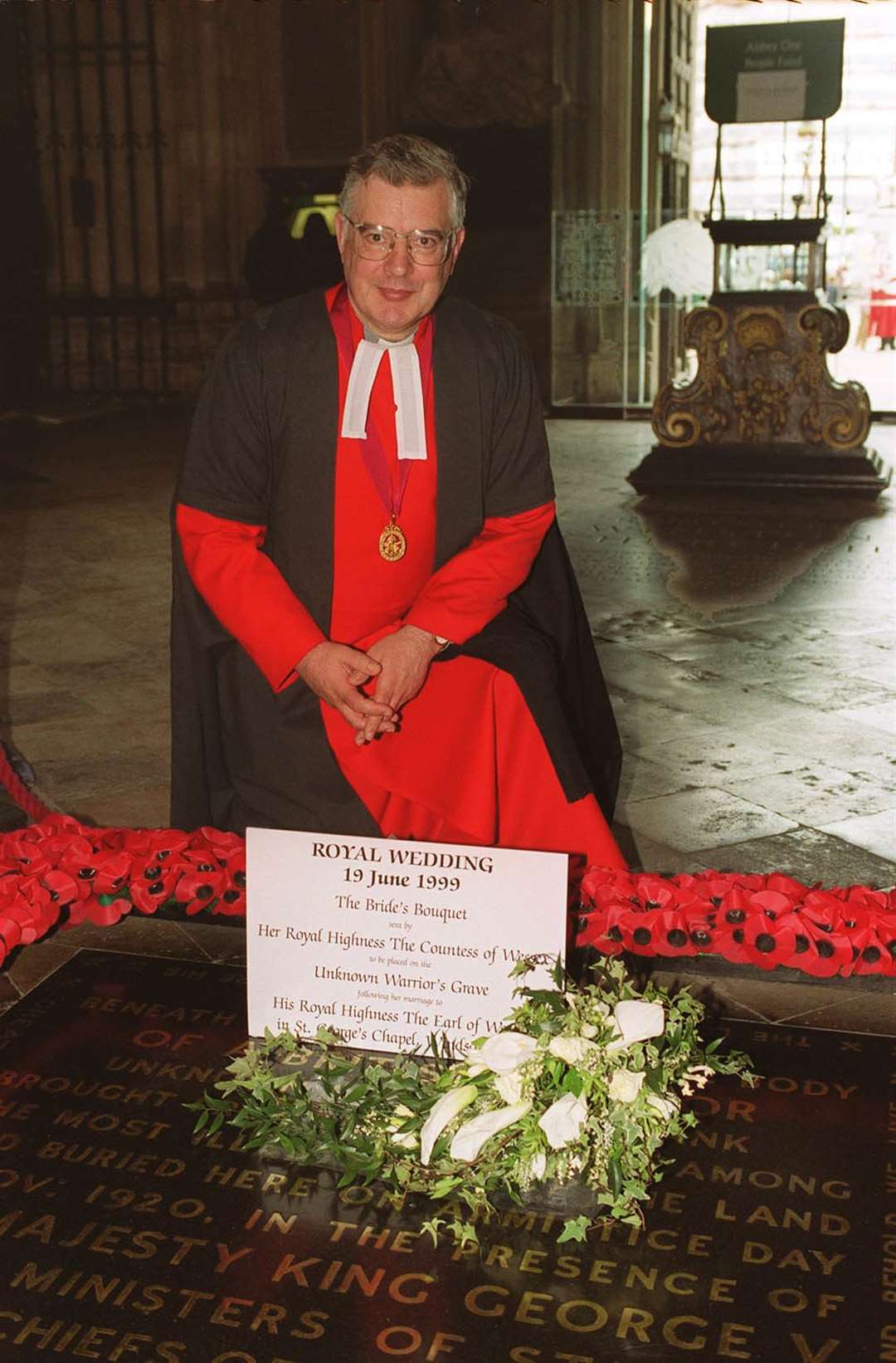 The Dean of Westminster Dr Wesley Carr kneels behind the bridal bouquet of the Countess of Wessex in 1999 (PA)