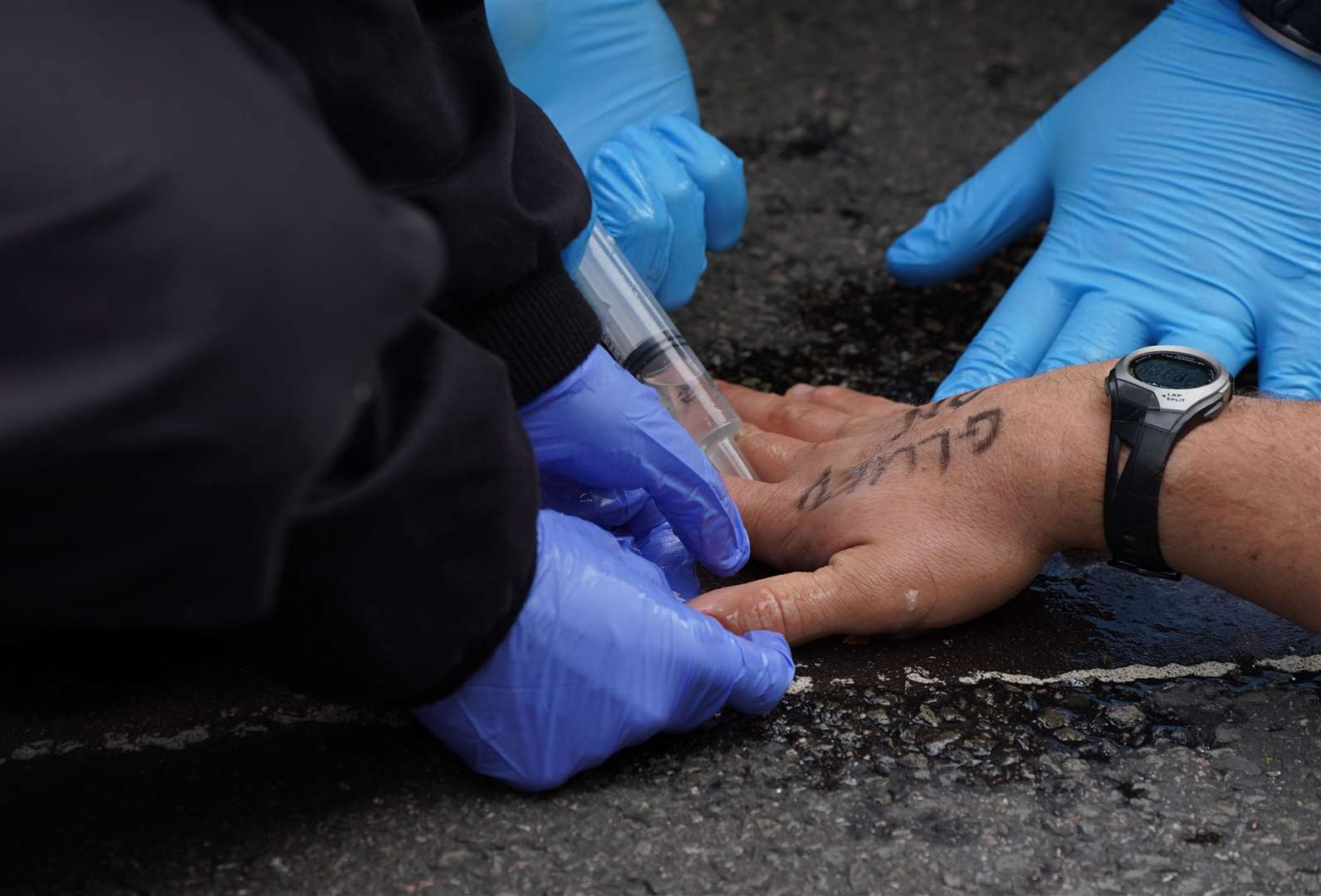 Police attempt to free a man who has glued himself to the road (Ian West/PA)