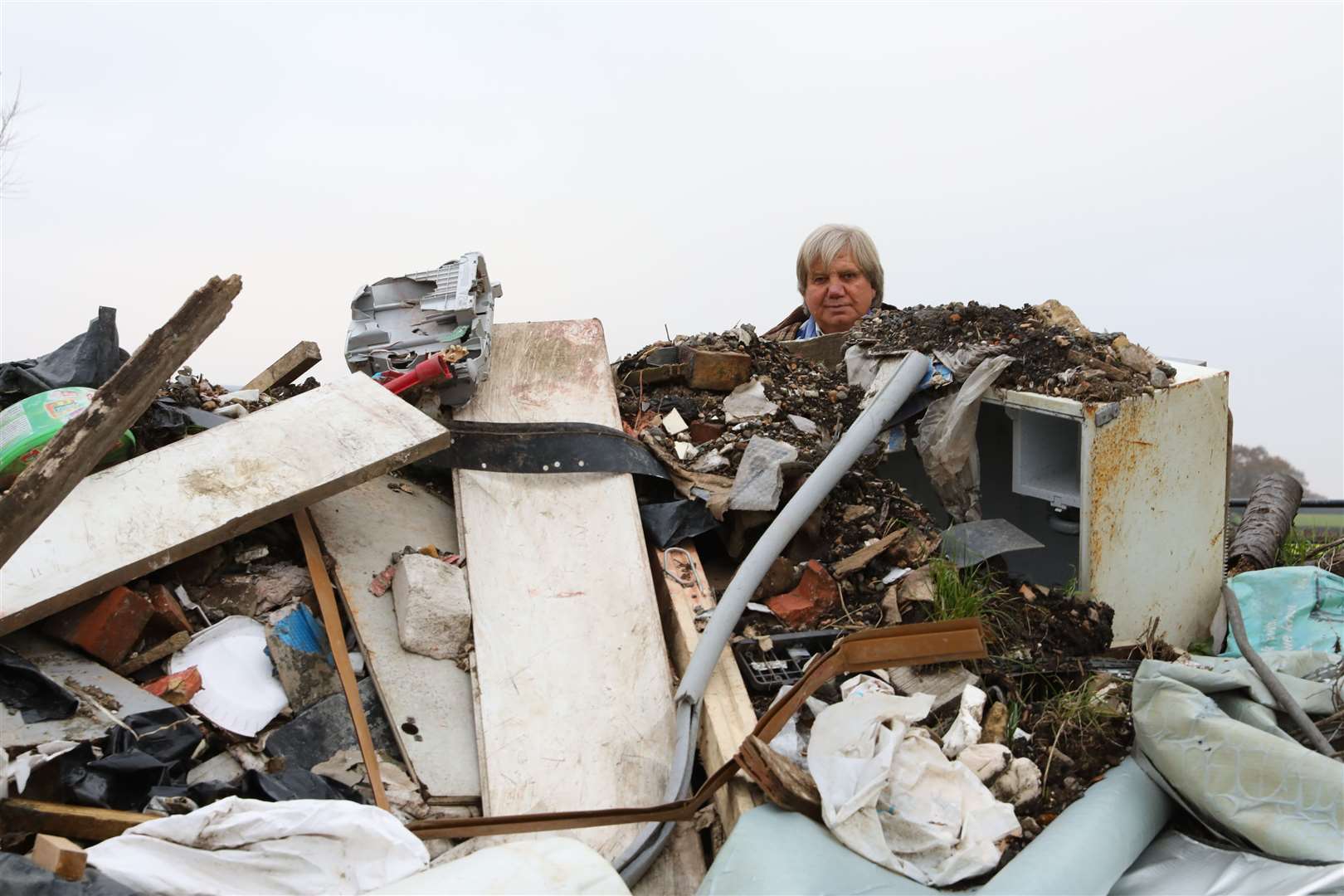 Pictured is Lester Gosbee peering over fly-tipped rubbish in Frittenden