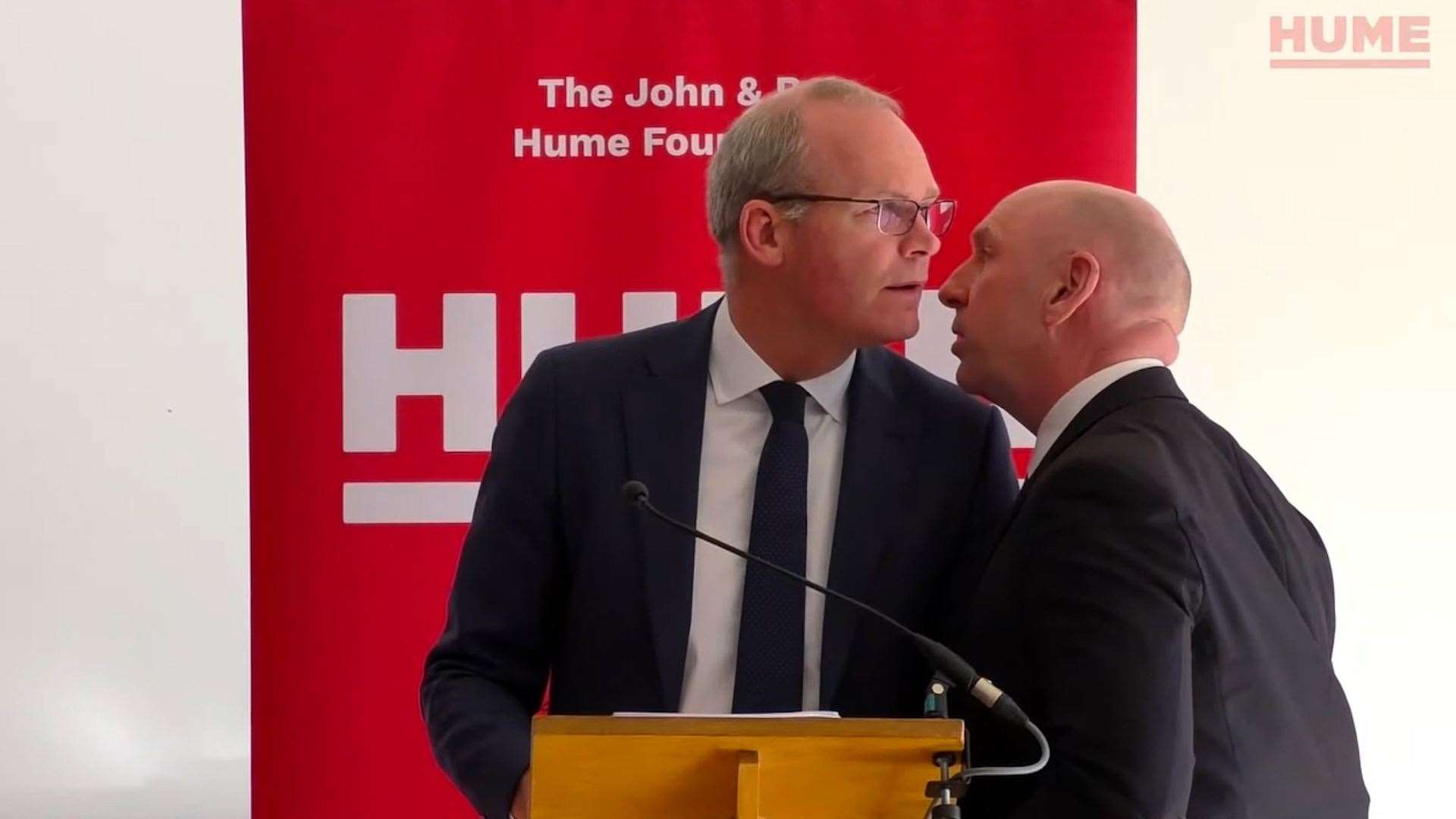 Simon Coveney is ushered from the room at The Houben Centre (Hume Foundation/PA)