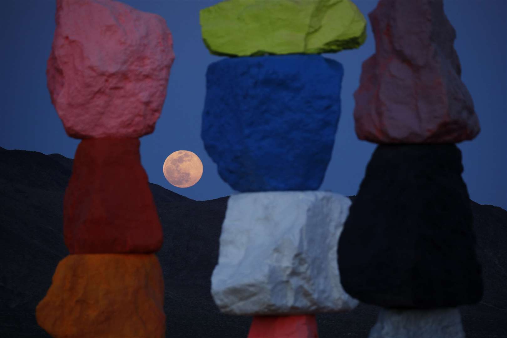 The supermoon rises behind the artwork titled Seven Magic Mountains in Las Vegas (John Locher/AP)