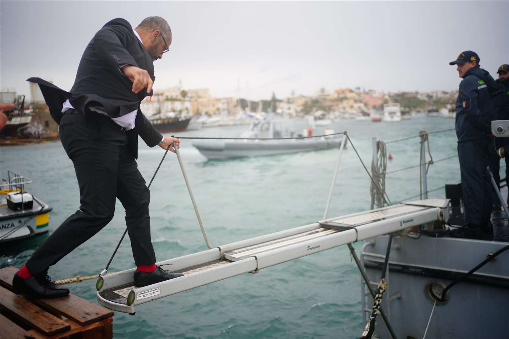 James Cleverly minds his step as he climbs onto a police boat in the Italian port of Lampedusa (Victoria Jones/PA)