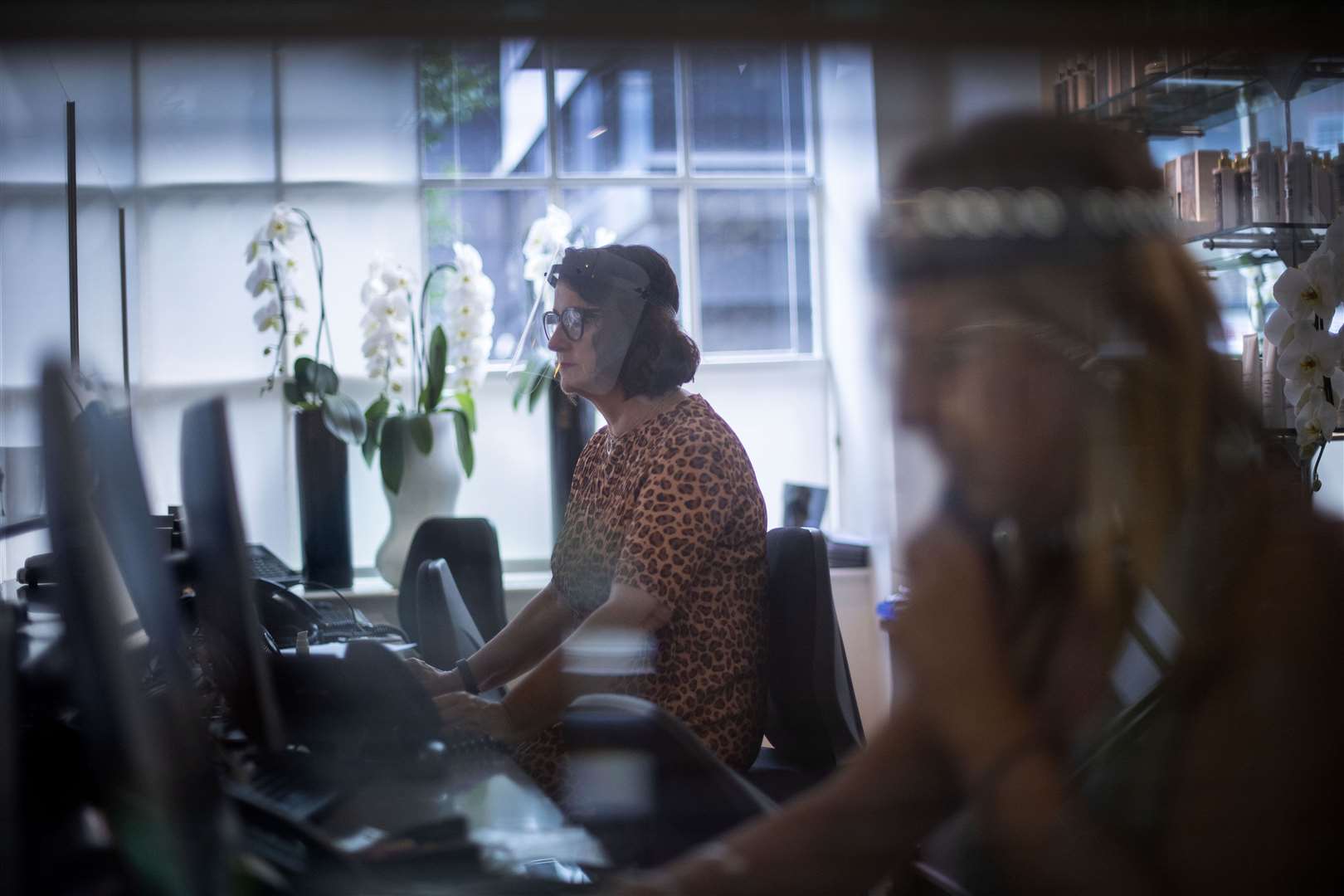 A receptionist at Daniel Galvin hairdressers wears a face shield and sits behind a protective screen (Victoria Jones/PA)