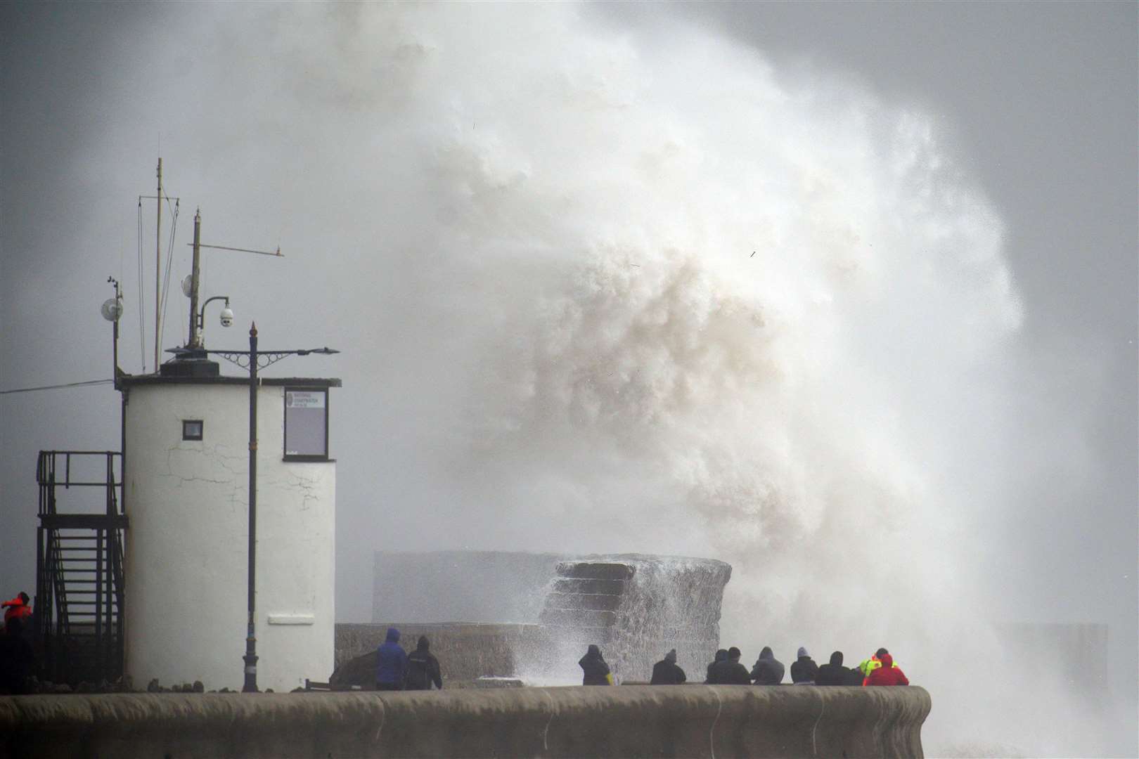 People watch as waves crash over the seafront in Porthcawl in Wales (Ben Birchall/PA)