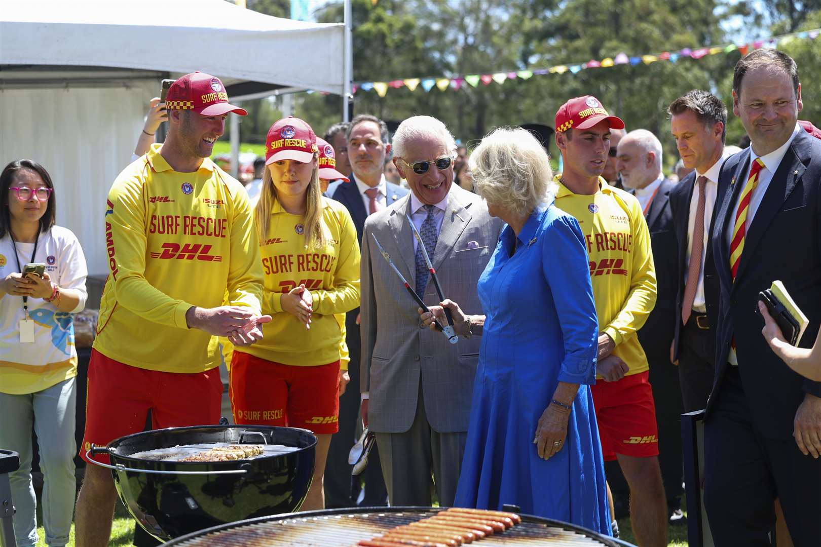 Charles and Camilla laugh as they turn some sausages during the community barbecue (Toby Mellville/PA)