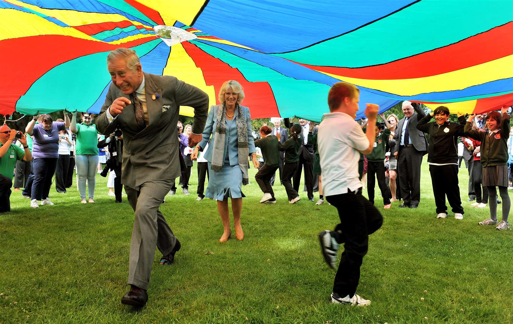 The Prince of Wales and the Duchess of Cornwall run under a brightly coloured parachute during a youth rally on their last visit to Guernsey in 2012 (John Stillwell/PA)