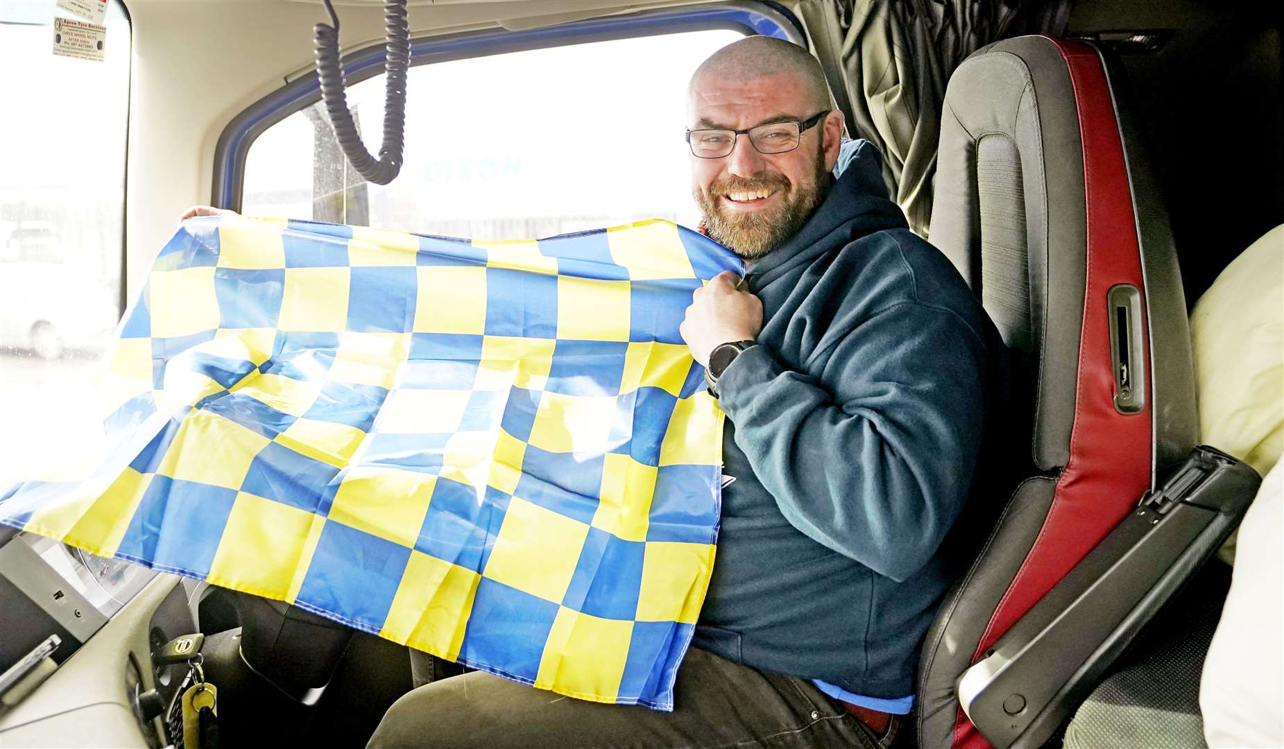 Truck driver Donal Lennon holds a flag in his cab as the Aid From Ireland lorries prepare to leave Dublin Port (Niall Carson/PA)